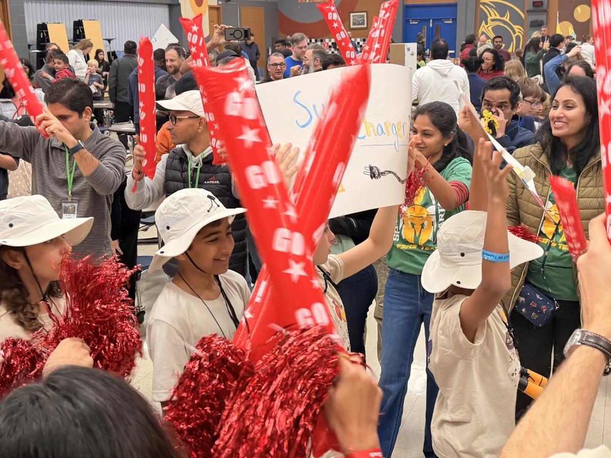 Students cheering their FIRST LEGO League team with pom-poms and a hand-made sign