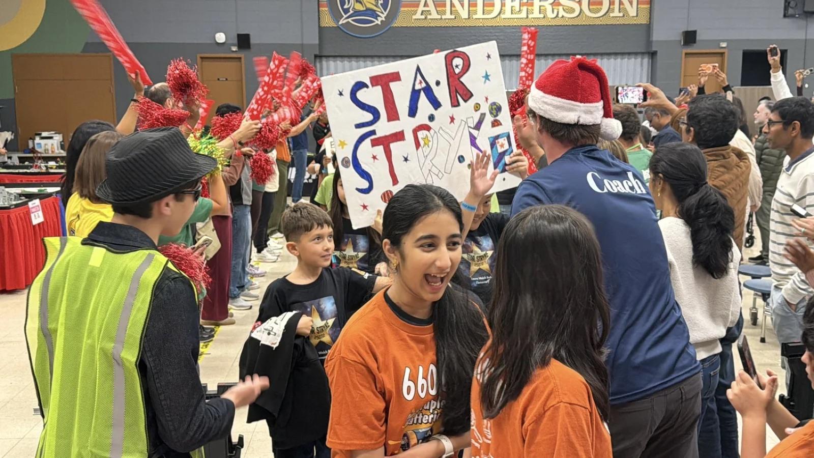 A FIRST LEGO League team in orange shirts celebrating with their Star Strike sign