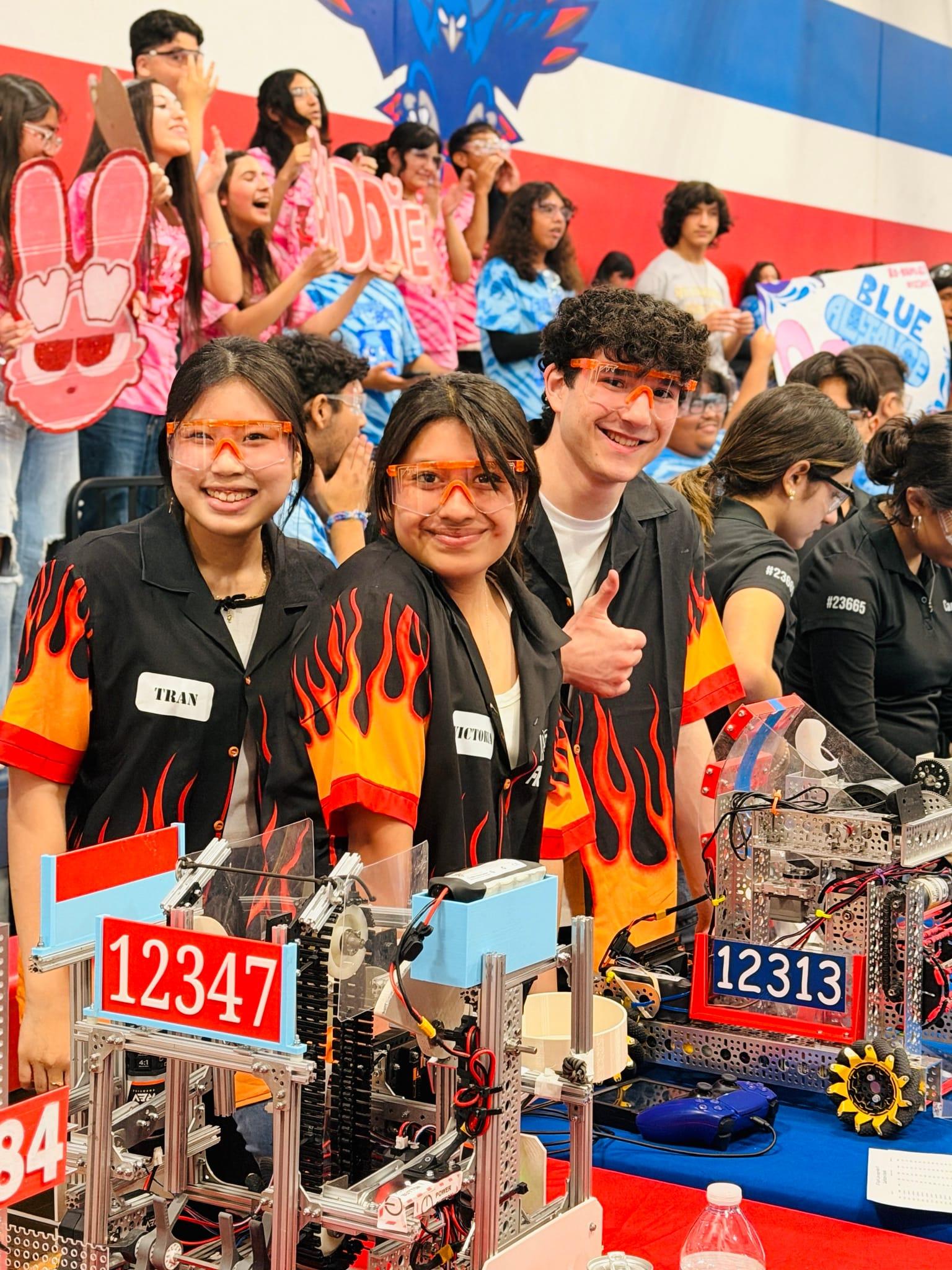 FIRST Tech Challenge team members in safety glasses and flame shirts smiling beside their robots in the pits, Harmony School of Excellence, South Texas 2026