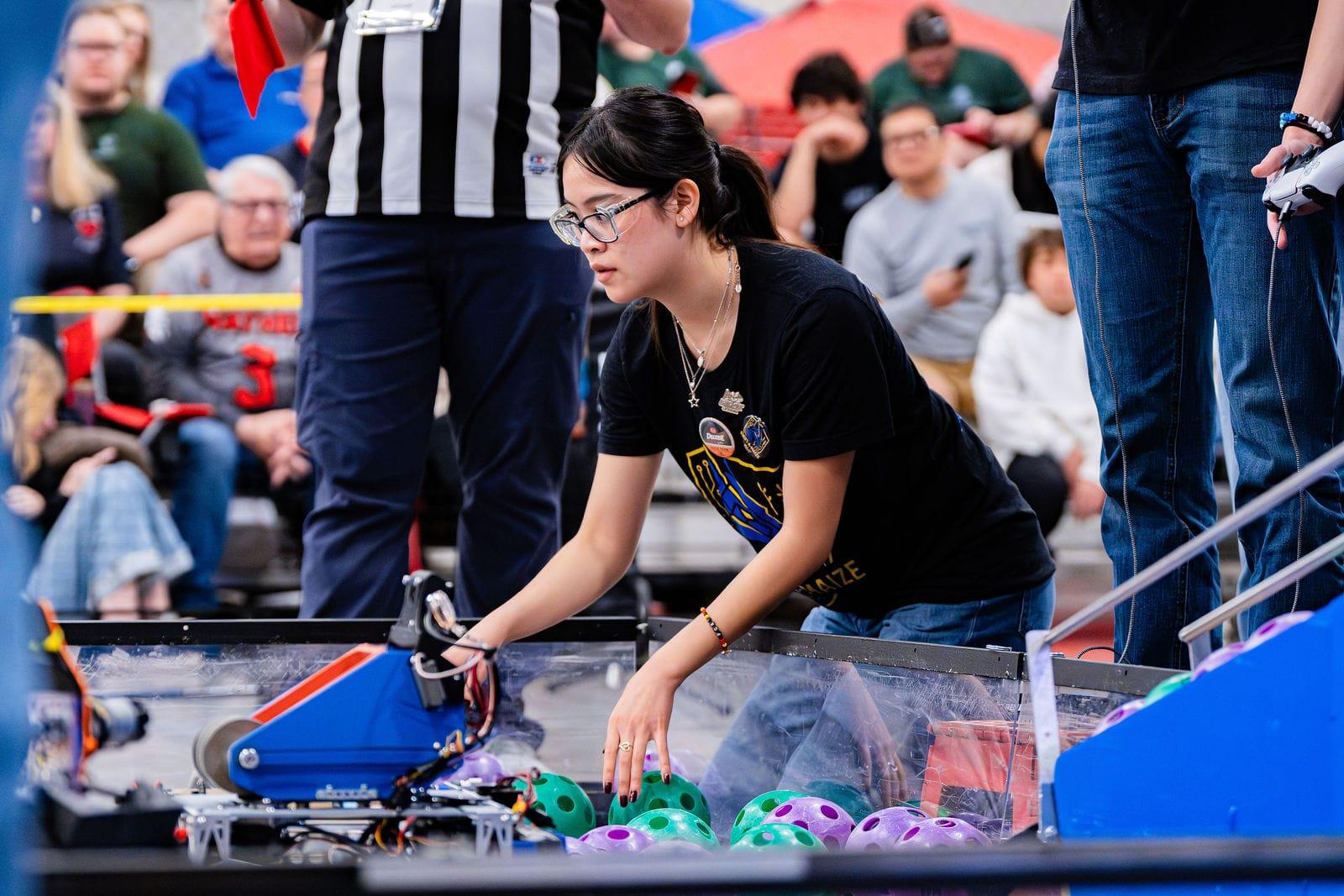 A FIRST Tech Challenge student setting her team's robot on the field among purple and green game pieces at the Texas Cup