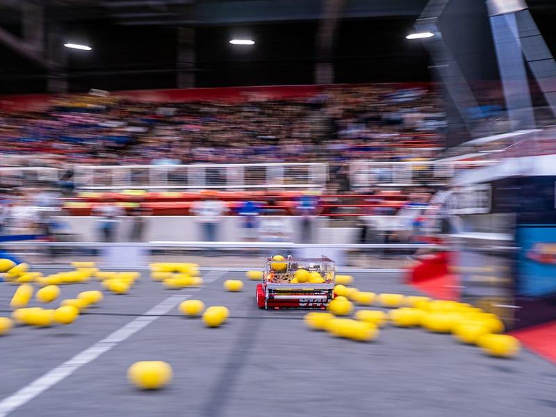 A FIRST Robotics Competition robot on a field scattered with yellow game pieces