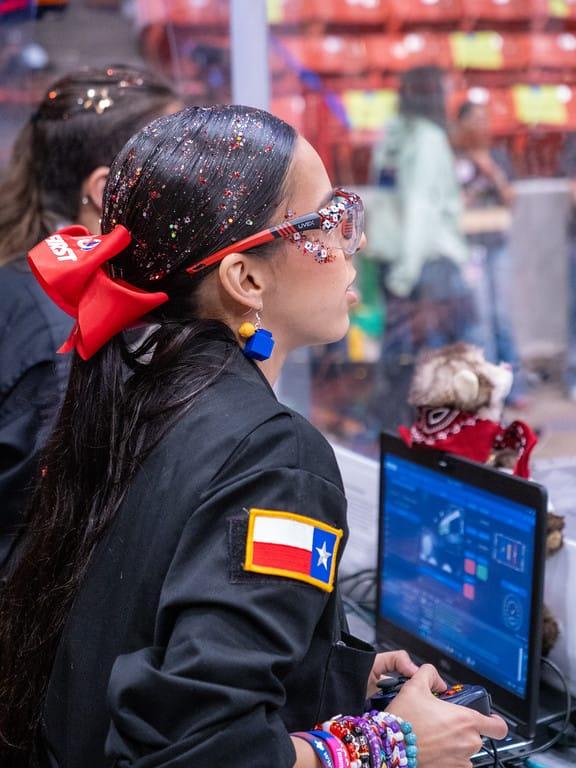 A FIRST Robotics Competition driver with a Texas flag patch on her sleeve at the controls during the District Championship